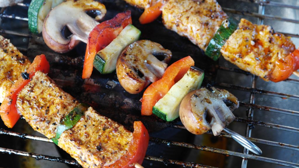 Skewers with mushrooms, zucchinis, bell peppers, and meat being grilled.